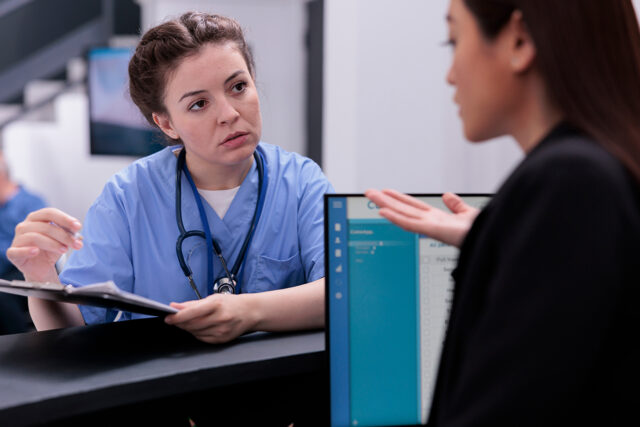 Front desk staff at a medical practice reviewing paperwork, causing a delay in patient check-in.