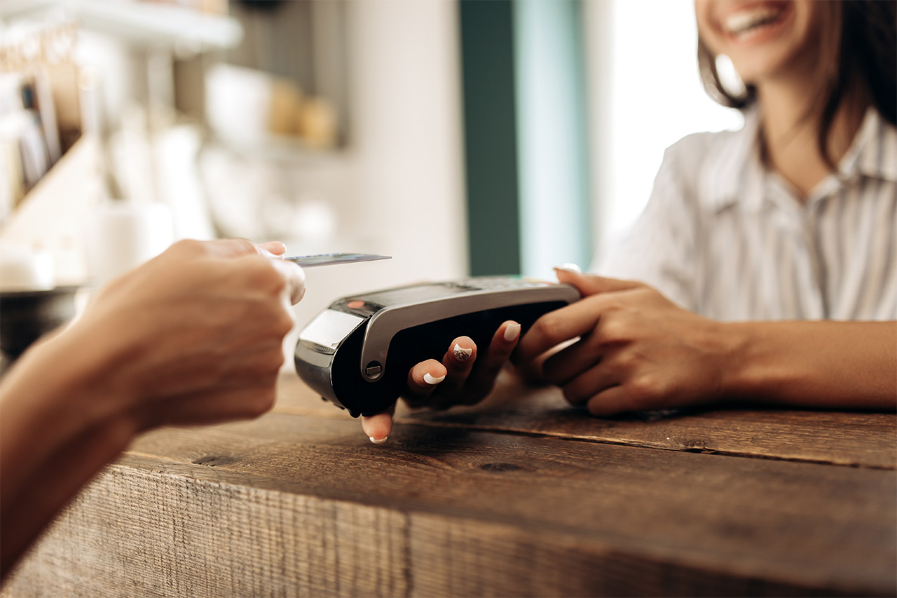 Patient making a contactless payment with a credit card at the front desk of a dental office, while the receptionist holds the payment terminal and smiles.