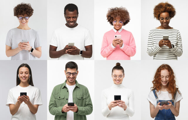 Row of diverse young adults smiling while using smartphones, standing against a light background.