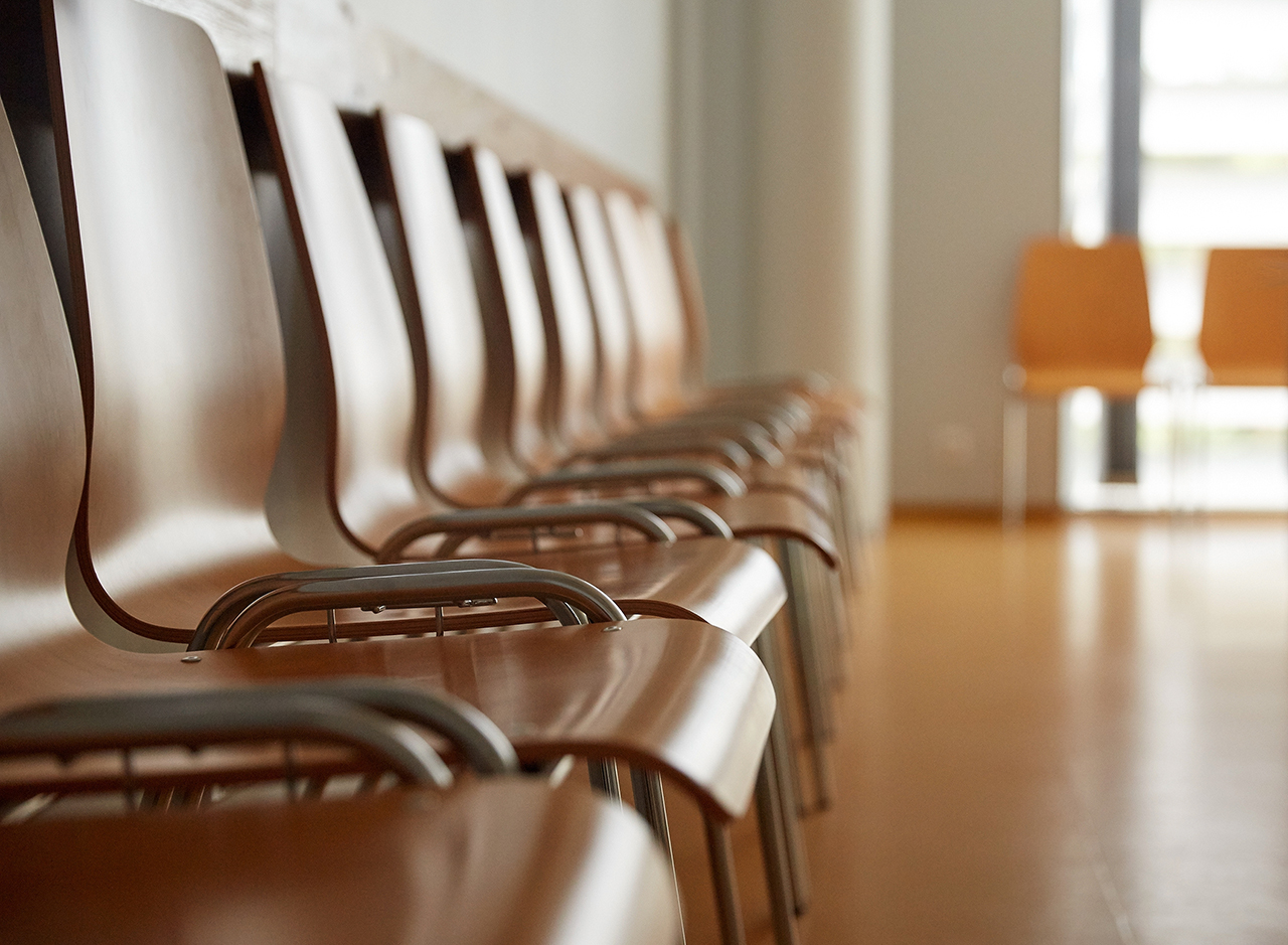 Row of empty wooden chairs lined up in a bright waiting room.