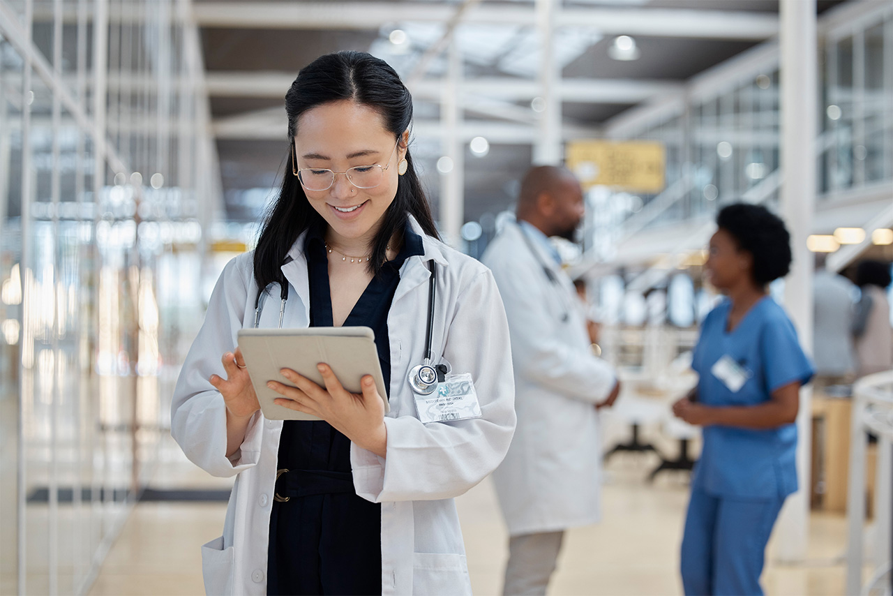 Healthcare professional reviewing information on a tablet in a clinical setting, representing the use of healthcare IT systems to manage data, workflows, and digital tools across a busy care environment.