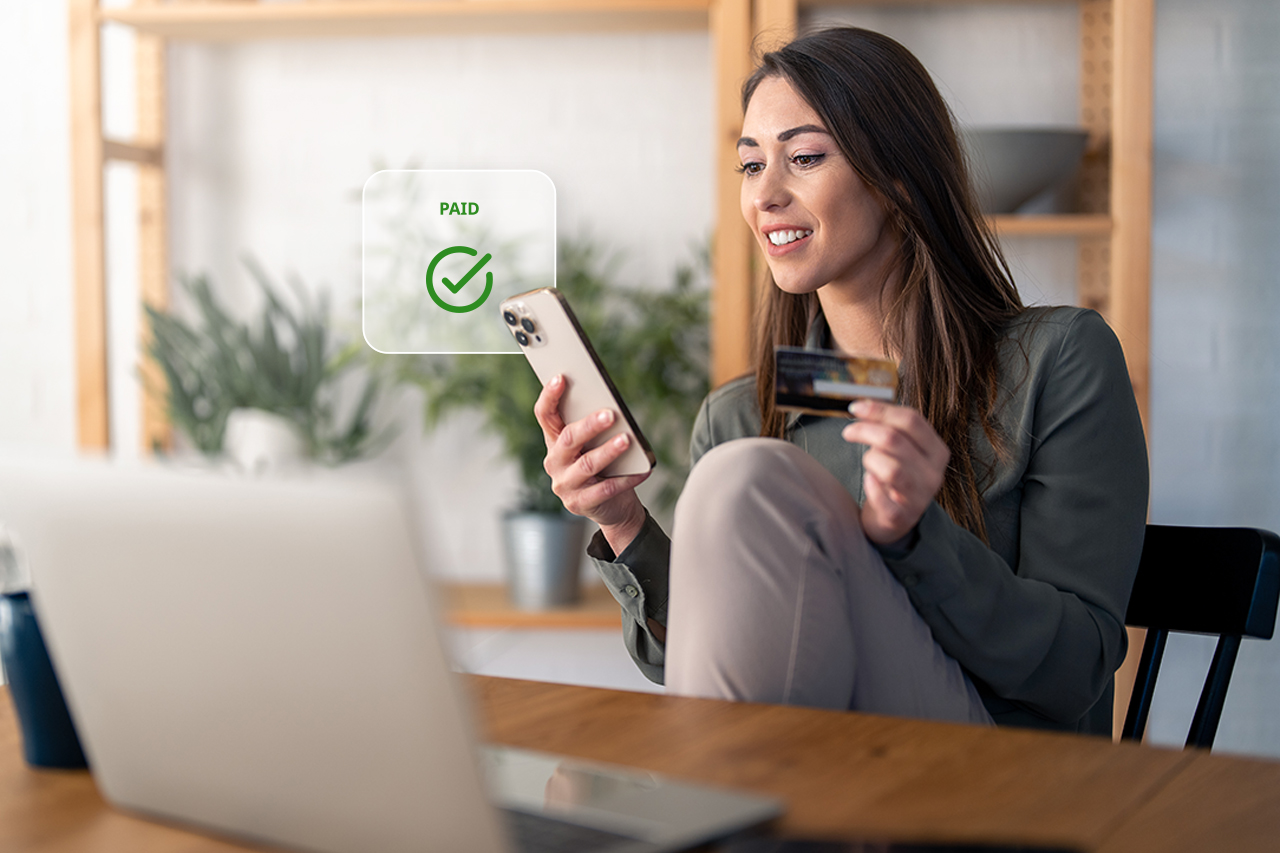 Woman smiling while viewing a payment confirmation on her smartphone and holding a credit card, with a “Paid” checkmark displayed on screen—illustrating clear patient communication, convenient billing, and strengthened patient loyalty through transparent digital payment experiences.