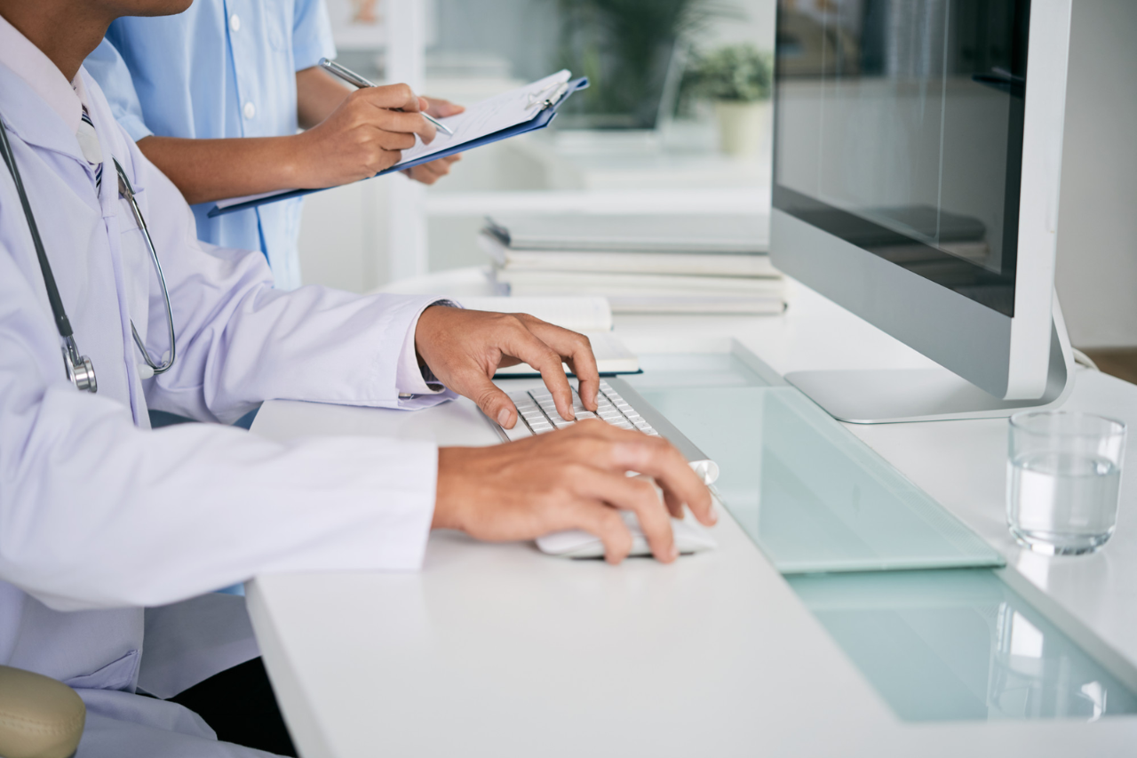 Doctor entering patient data on a computer while colleague writes notes in a modern medical office