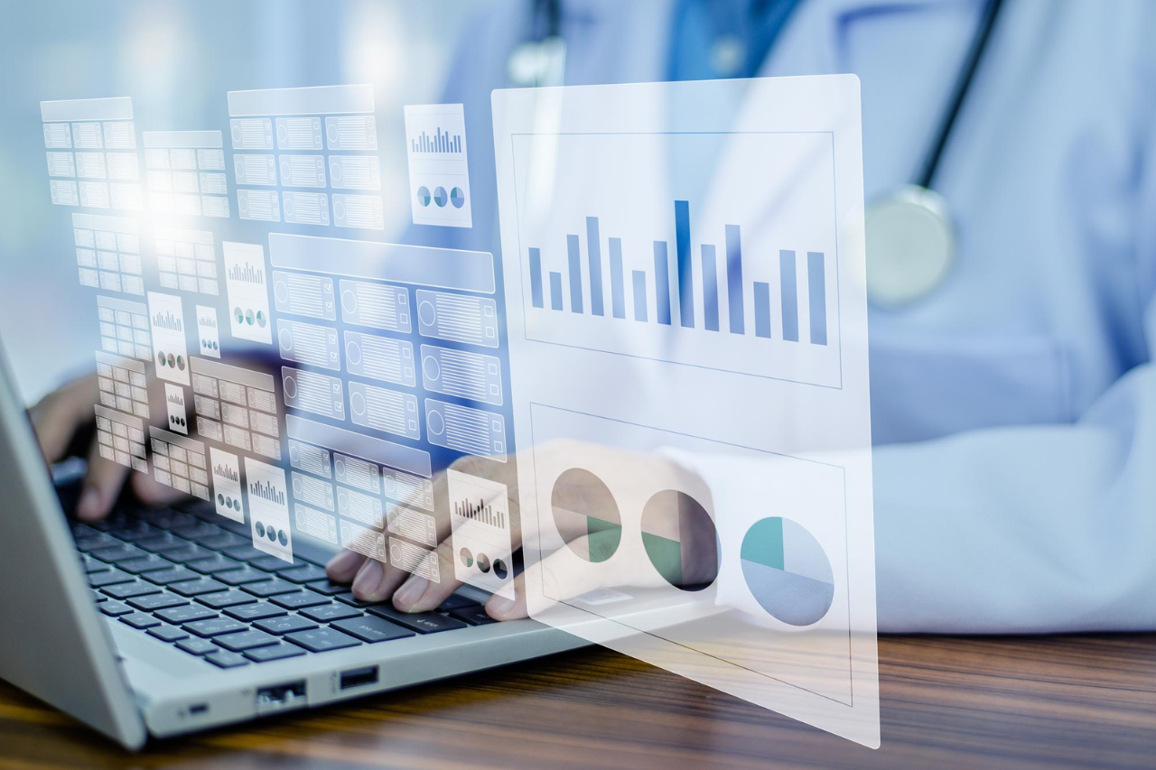 Healthcare professional using a laptop with digital analytics dashboards and charts overlaid on the screen.