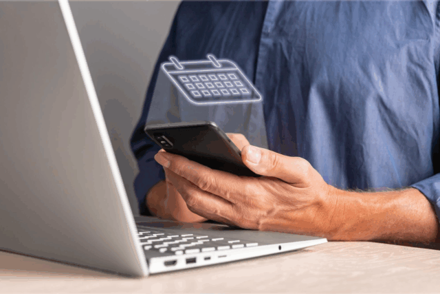 Person holding a smartphone next to a laptop with a digital calendar icon hovering above the phone screen.