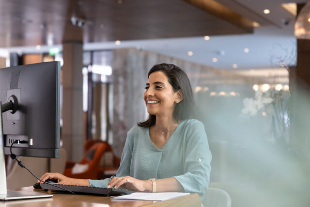 Front desk team member smiling at her computer as Solutionreach Virtual Scheduling Assistant helps the practice manage scheduling and reduce missed patient calls.