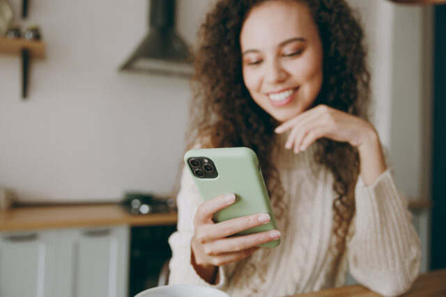 Patient smiles while using her phone to respond to a Solutionreach recall message and reconnect with her practice.