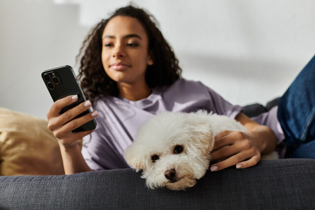 A patient relaxes at home with her dog while using her phone, staying connected to her dental practice through Solutionreach recall communication.